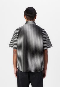 Short-sleeve shirt with black and white stripes, featuring a collared neckline and relaxed fit. Material appears lightweight with a smooth texture.
