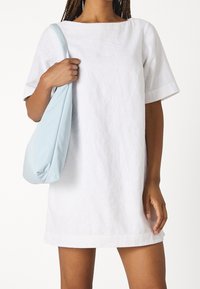 Vestido de lino blanco con mangas cortas y escote barco, combinado con un bolso suave y ligero en azul claro, llevado al hombro.