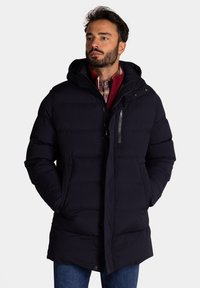 Marineblauwe pufferjas met een capuchon, ritssluiting en drukknoopsluiting, zijzakken, gequilt textuur en een iets langere snit. Casual look.
