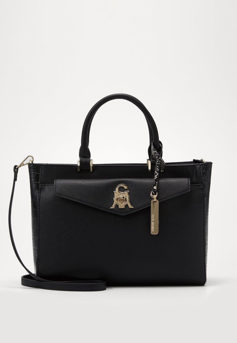 Sac à main structuré noir avec doubles poignées, poche avant à rabat, logo doré de la marque et bandoulière amovible sur fond uni.