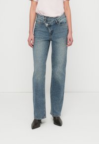 Μπλε τζιν κατευθείαν γραμμή με μεσαίο ύψος μέσης, διαθέσιμα με πέντε τσέπες και ορατή ραφή. Συνδυασμένα με μαύρες μπότες με μυτερή μύτη.