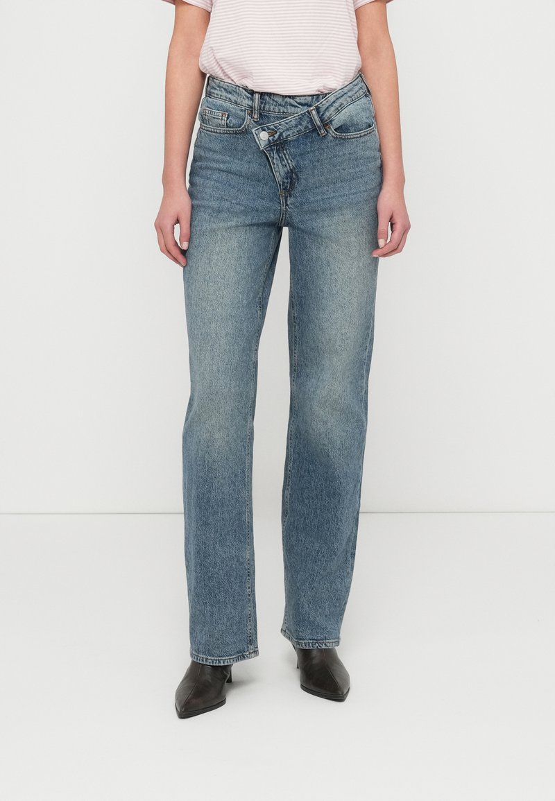 Μπλε τζιν κατευθείαν γραμμή με μεσαίο ύψος μέσης, διαθέσιμα με πέντε τσέπες και ορατή ραφή. Συνδυασμένα με μαύρες μπότες με μυτερή μύτη.