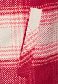 Red and pink plaid fabric with a soft texture, featuring a white accent piece. The pattern includes woven checks and stripes.