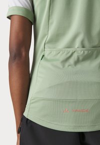 Vaaleanvihreä urheilupaita, jossa on struktuurinen kangas, lyhyet hihat ja kaareva helma. Paidassa on vaaleanpunainen VAUDE-logo alhaisella selkäosalla.