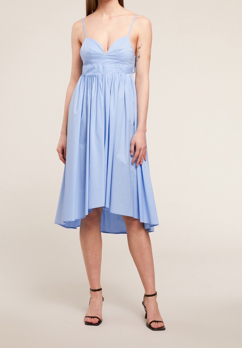 Robe bleu clair, longueur genou, avec un corsage ajusté, un décolleté en V et une jupe froncée. Fines bretelles et une ourlet arrière légèrement plus long. Texture lisse.