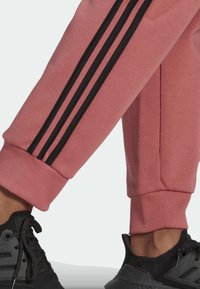 Roze sportieve joggings met zwarte zijstrepen, afgewerkte enkels en een zachte textuur, gecombineerd met zwarte sneakers met gestructureerde zolen.