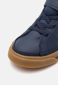 Baskets en cuir bleu marine avec une semelle en caoutchouc naturel, dessus texturé avec des lacets et un col rembourré. Vue rapprochée mettant l'accent sur la zone des orteils.
