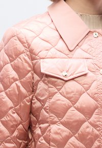 Ροζ μπουφάν με καπιτονέ ύφασμα και ομαλή υφή, που διαθέτει μυτερό γιακά, τσέπη με καπάκι και κουμπώματα με λαμπερά κουμπιά.
