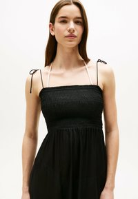 Zwarte strapless jurk met een gerimpeld lijfje, verstelbare bandjes en een vloeiende rok. Gladde textuur met een lichtgewicht stof.