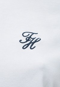 Λευκό βαμβακερό πουκάμισο με μπλε κεντημένο μονόγραμμα "F&H" στην αριστερή περιοχή του στήθους. Λεία υφή με κλασικό στρογγυλό λαιμόκοψη.