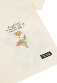 Camicia color crema con testo ricamato verde "associazione alpinistica dente di leone" e un fiore di dente di leone ricamato sopra un'etichetta nera "Flower Mountain Universal Works".