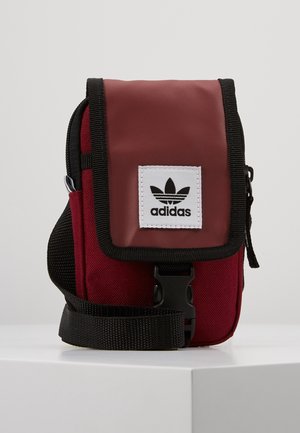 Mała bordowo-czerwona torba na ramię Adidas z czarną lamówką, regulowanym paskiem, przednią klapką i białą naszywką z logo.