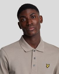 Polo beige hecho de algodón texturizado, con una tapeta de tres botones y un logo bordado amarillo en el lado izquierdo del pecho.