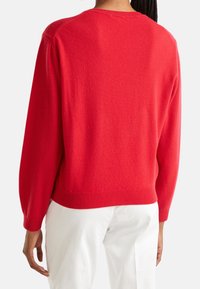 Punainen neulottu villapaita, jossa pyöreä pääntie ja laskeutuvat olkasaumat. Pehmeä rakenne, resorireunus helmassa ja hihoissa. Kuvassa paita takaa päin.