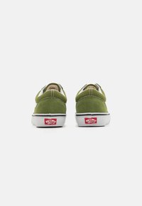 Gröna mocka låga sneakers med vita gummisol, med bakre logotypdetaljer i rött. Designen inkluderar kontrasterande sömmar.