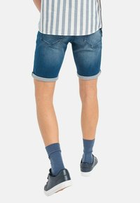 Shorts de mezclilla en azul oscuro con dobladillos enrollados, que cuentan con bolsillos traseros y una textura suave. Combinados con zapatillas oscuras y calcetines azules.