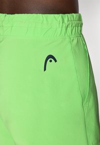 Neon-grüne Shorts aus leichtem Material mit einem elastischen Bund. Mit einem dunklen Logo auf der linken Seite und Seitentaschen.