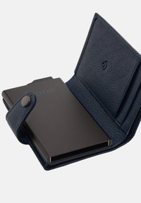 Tumši zila ādas maku ar pogu aizdari, kas iekļauj strukturētu iekšpusi, metāla aksesuārus un melnu kartes turētāju iekšpusē.