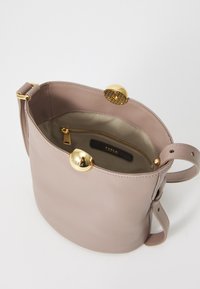 Borsa a mano rotonda in pelle rosa chiaro con chiusura in metallo dorato, tasca con zip all'interno e tracolla regolabile. Texture liscia e design minimalista.
