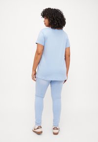 Camiseta de manga corta azul claro con dobladillo redondeado, combinada con jeans ajustados azul claro y zapatillas casuales crema con acentos marrones.
