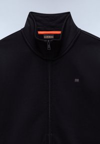 Veste noire zippée avec col montant, petit logo sombre sur la poitrine, et bande intérieure contrastante orange au niveau du col.