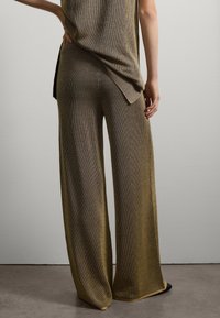 Conjunto de punto grueso en una combinación de colores dorado y marrón. La parte superior presenta un dobladillo trasero más largo. Los pantalones de pierna ancha tienen un ajuste holgado y textura acanalada.