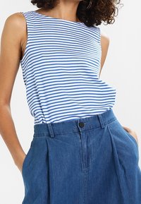 Blauw en wit gestreepte mouwloze top gemaakt van zachte stof, gecombineerd met een high-waisted blauwe denimrok met voorplooien en zakken.