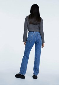 Jeans azules de talle alto con pierna recta, que incluyen bolsillos traseros y cremallera. Combinados con un suéter gris ajustado de canalé y zapatos de plataforma negros.