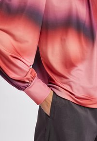 Sidenblus med en gradient från rosa till lila, med ballongärmar och rynkade manschetter. Kombinerad med mörkgrå byxor.