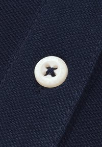 Niebieska próbka materiału z teksturowanym splotem, z okrągłym, kremowym guzikiem z czterema dziurkami i wytłoczonym logo marki.