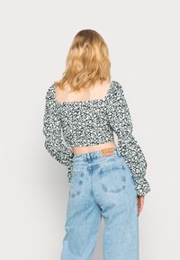Top floral curto com mangas bufantes, apresentando um fundo preto com flores brancas e verdes. Combinado com jeans claros de cintura alta.