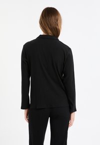 Czarny żeberkowany żakiet z kołnierzem, długimi rękawami i prostym krojem. Tkanina ma gładką fakturę z pionowymi liniami i minimalistycznym wzornictwem.