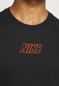 Černé bavlněné tričko s kulatým výstřihem a kr átkým rukávem, se vyšívaným oranžovým logem "NIKE" na prsou.