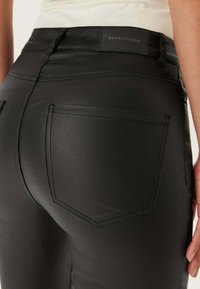 Zwarte faux leren broek met een getailleerd ontwerp, voorzien van gedetailleerde stiksels en een achterzak. Het merklabel "BUBBLEROOM" is zichtbaar.