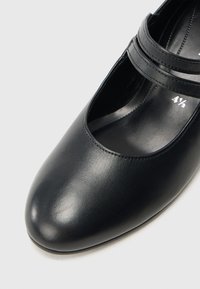 Musta nahkainen Mary Jane -tyylinen kenkä, jossa pyöreä kärki ja kaksi ohutta hihnaa päällä. Sileä pinta ja pehmustettu sisäpohja. Koko merkitty sisäpuolelle.