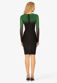 Langermige jurk met groene decoratieve bovenkant voorzien van studs, overgaand in een effen zwarte rok, strakke pasvorm met een ritsluiting.
