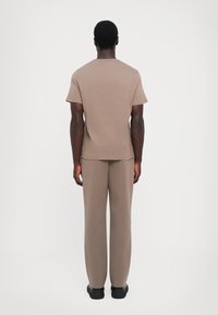 Lys brun strikket t-skjorte og matchende bukser, begge med en avslappet passform. Stoffet virker mykt og glatt, designet for komfort og enkelhet.