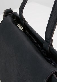 Svart läderhandväska med strukturerad yta, dubbla handtag och dragkedjestängning med en silverfärgad dragfläkt. Enkel, rektangulär design.