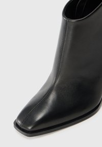 Black leather ankle boot with a pointed toe and smooth texture. Features a minimal seam design and a flat, sleek rubber sole.