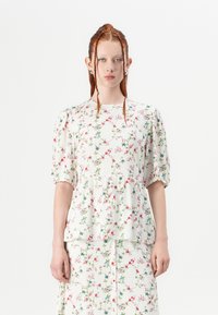 Top peplum floreale in tessuto leggero, con maniche corte a sbuffo e uno sfondo bianco decorato con motivi floreali colorati.