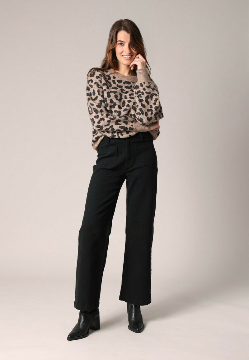 Beige luipaardprint trui, zwarte wijde broek, en zwarte hak enkellaarsjes. Zachte textuur, ontspannen pasvorm en opvallende patronen op de trui.