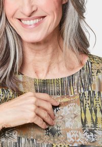 Multi-patroon blouse met aardetinten, ronde halslijn en subtiele texturen. Patronen omvatten geometrische en organische vormen.