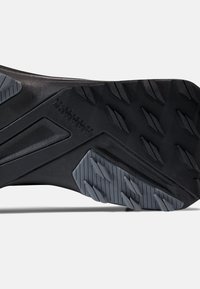 Svart gummiyttersula med texturerad mönstring och ljusgrå accenter. Har vinklade design detaljer för förbättrat grepp och stabilitet.