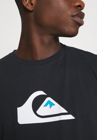 Black cotton t-shirt featuring a large white and blue wave and mountain logo on the chest, with a crew neck and short sleeves.