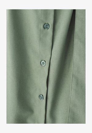 Grøn stofskjorte med en glat tekstur, knaplukning med lyseblå knapper og diskret syning langs stolpen.