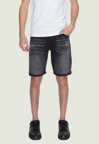 Pantaloni shorts in denim nero con risvolti, caratterizzati da una finitura sbiadita. Indossati con una maglietta bianca semplice e sneakers nere.