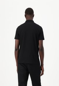 Black polo shirt made of cotton with a classic collar and short sleeves. Features a subtle logo on the upper back. Smooth texture.