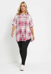 Camisa de cuadros rosa y blanca con mangas cortas arremangadas, botones delanteros y dobladillo curvado, combinada con pantalones negros y zapatillas blancas.
