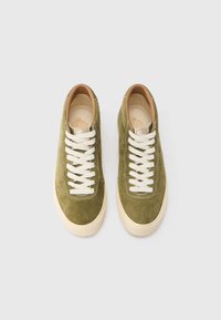 Zaļas zamšādas augstās tenisa kurpes ar baltām šņorēm, brūngani ieliktnēm un apaļu purngala dizainu, ar smalkām šuvju detaļām.