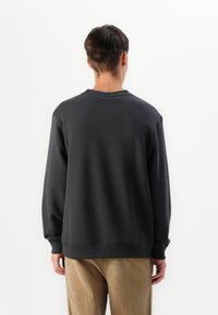 Dark gray sweatshirt with a crew neckline and ribbed cuffs, paired with light beige corduroy pants. Smooth texture, minimalist design.